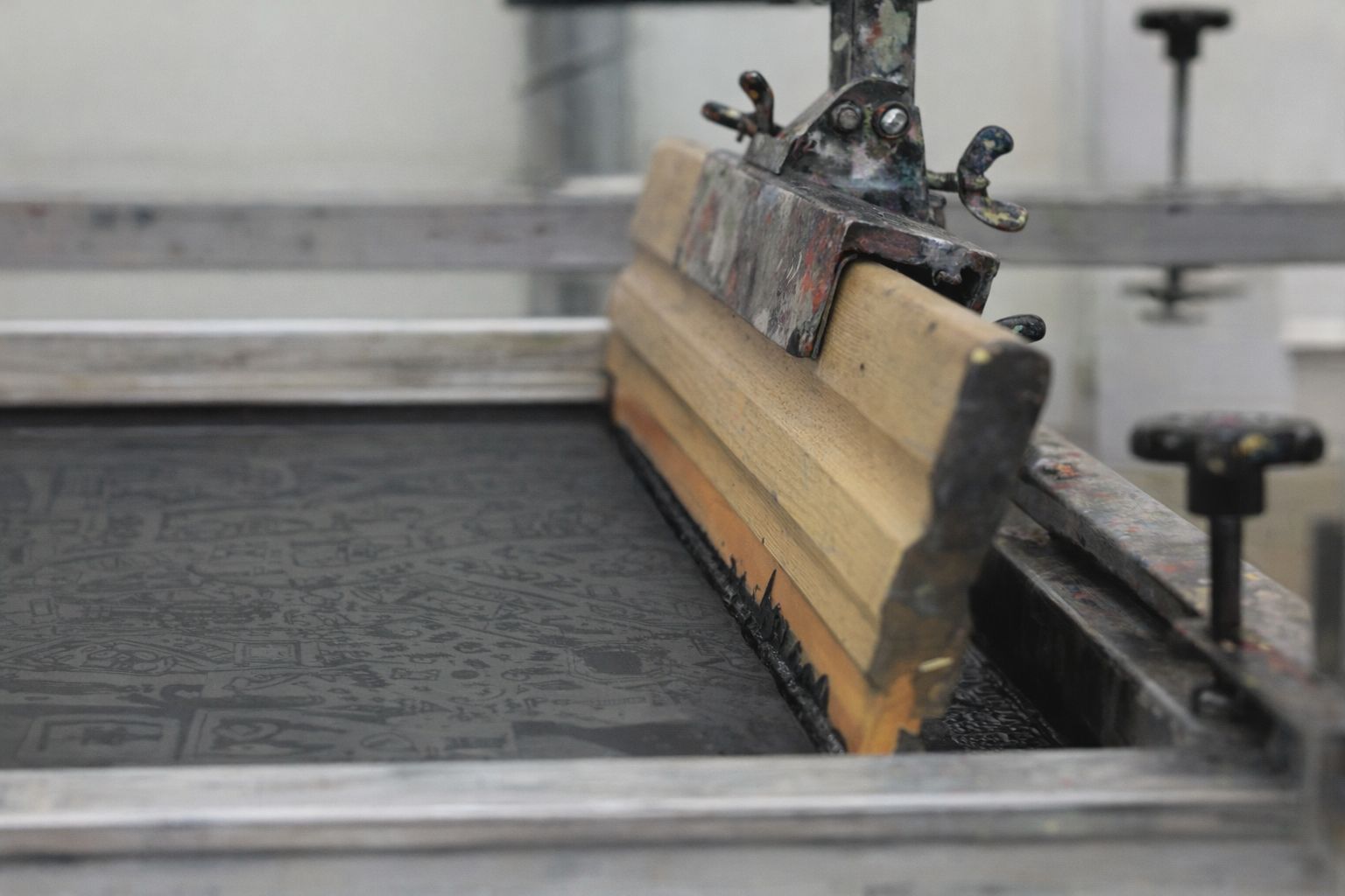 En rakel av trä som pressar färg genom en screentrycksram.